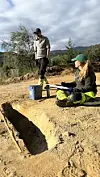 To personar arbeider ved ei utgravingsgrop med spann og arbeidsutstyr.
