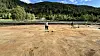To personar står på ein open grusplass med skogkledde åsar i bakgrunnen.