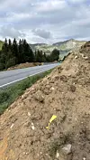 Asfaltert veg gjennom skog og fjell, med ein jordskråning i forgrunnen.