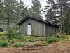 Grønmåla treskur med raudt tak står mellom tre i skogen.