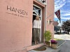 Person står i døropninga til Hansen Kafé & isbar, med blomar og norsk flagg utanfor.