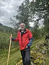 Mann i raud jakke med trestav på ein skogssti.