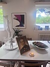 Spisebord med innramma portrett, fruktfat, lys og kunstverk i ei lys stove.
