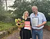 To personar står i ein hage med blomar og innramma dokument.