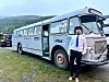 Mann står framfor ein lyseblå veteranbuss på ei grasmark.