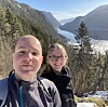 To personar tek selfie framfor ein fjord mellom snødekte fjell.
