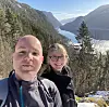 To personar tek selfie framfor ein fjord mellom snødekte fjell.