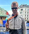 Mann med solbriller held ein medalje ved eit byløp i ein by.