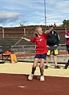 Kvinne i raud drakt held ein kastestav på ei friidrettsbane.