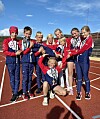 Unge friidrettsutøvarar i raude og marineblå drakter poserer med medaljar på bana.