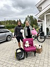 To kvinner står ved ein rosa stol med ein liten hund utanfor eit hus.