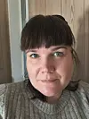 Portrett av ein person i grå strikka genser framfor ein trevegg.