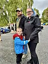 To vaksne og eit barn står saman på ein parkeringsplass.