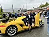 Mann står ved ein gul sportsbil med open dør på eit utandørs biltreff.