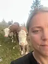 Kvinne nær kamera med fleire storfe på grasmarka bak seg.