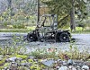 Opent terrengkøyretøy står på grus mellom skog og fjell.