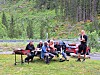 Gruppe menneske sit ved eit bord medan ein person står framfor dei i skogkanten.