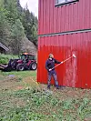 Person spyler ein raud trevegg medan ein traktor står i bakgrunnen.
