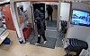 Fleire personar står ved inngangen til ein butikk, med ein skjerm og stolar på høgre side.