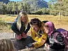 Tre personar ser saman på ein mobiltelefon ved ein trebenk i skogen.