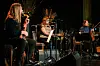 Tre musikarar spelar på ei scene med gitar, perkusjon og mikrofonar.