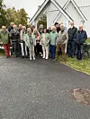 Gruppe vaksne står samla framfor ein kvit trebygning.