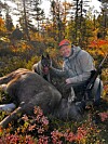 Person med jakthund ved ein felt elg i haustfarga skog.