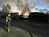 Brannmann står ved slangar medan bygningar brenn i bakgrunnen.
