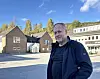 Mann i mørk jakke står på ein skuleplass framfor murbygningar.
