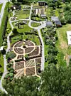 Flyfoto av ein geometrisk hage med sirkelforma bed, gangar og frodig vegetasjon.
