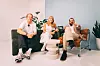 Tre personar sit i stolar rundt eit lite bord i eit lyst studio.