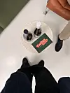 Rundt bord med flasker og brosjyre, sett ovanfrå mellom fleire personar.