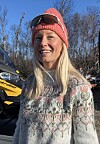 Kvinne i raud lue står ved ein gul og svart Ski-Doo-snøskuter i skogen.