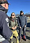Tre personar står saman på ein parkeringsplass i solskin.