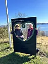 To kvinner står bak eit informasjonsskilt ved ein innsjø.