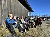 Gruppe menneske sit i graset ved ein trevegg, fleire med sykkelhjelm.