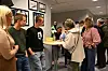 Menneske står rundt eit høgt bord og snakkar i eit innandørs lokale.