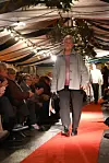 Kvinne i grå jakke går på raud catwalk framfor sitjande publikum.