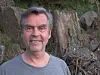 Portrett av ein mann framfor ein trestomn og steinar utandørs.